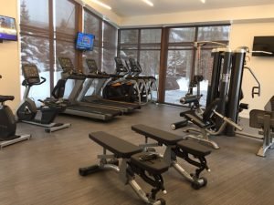 A windowed corner of a room with Cardio and weight training fitness equipment