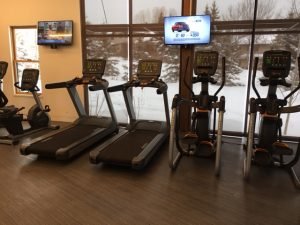 Two TVS with ellipticals, treadmills and bikes underneath