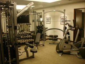 A mirrored residential fitness room with ellipticals and weights