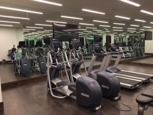 A mirrored room with a TV and multiple treadmills and ellipticals